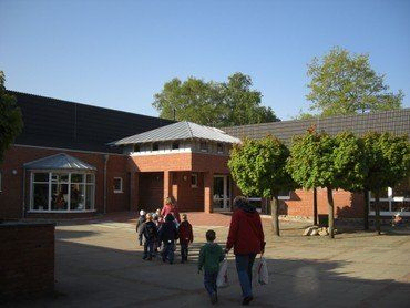 Kinder betreten die Evangelische Kindertagesstätte Kinderarche Büdelsdorf an einem sonnigen Tag.